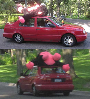 Red Jetta car with a brown and hot pink giant monkey tied to the roof