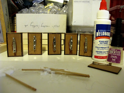 Row of brooches, showing the backs with pins just glued on, next to two bottles of glue.
