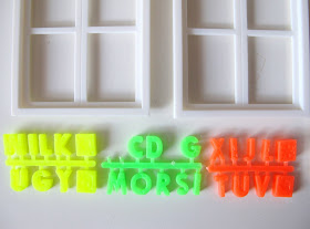Three sets of coloured plastic letters, arranged under two dolls' house miniature windows.