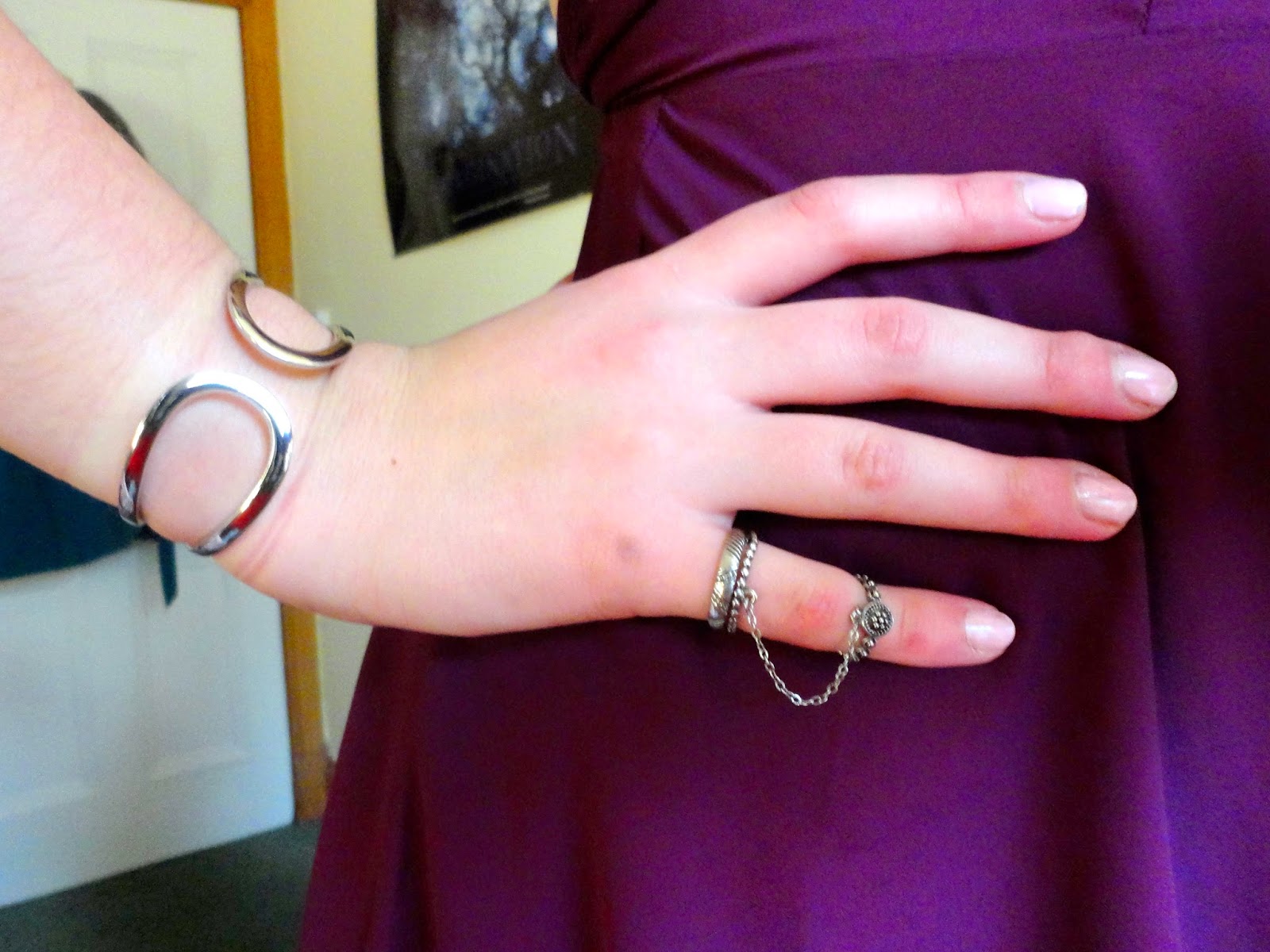silver metal bracelet and double chained rings, with pink nail polish over purple dress