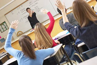 children in a classroom raising their hands to answer a question from the teacher