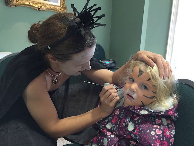 Tin Box Tot having her face painted as a tiger by a witch