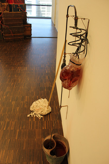Alison Saar - Exhibit at Figge Museum Photograph by Robin Peters of Glass Boxing Gloves 3/4 full of red liquid, a mop and a bucket with a metal tube draining the liquid downward.