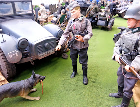 1/6 scale German soldier scolding a dog that has stolen sausages in a diorama of an army post on display at a scale model exhibition.