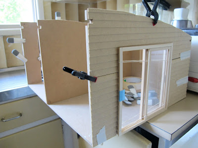 Wall and floor pieces of a doll's house kit taped into place, with siding clamped on and sliding doors installed.