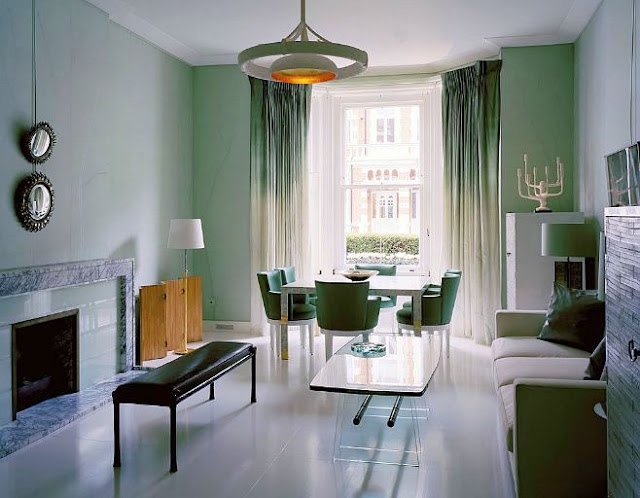 Alternative view of the living room with sea foam walls, matching ombre curtains, sea foam chairs, a tile  fireplace with a marble mantel, a black leather ottoman, a white sofa and coffee table with clear legs