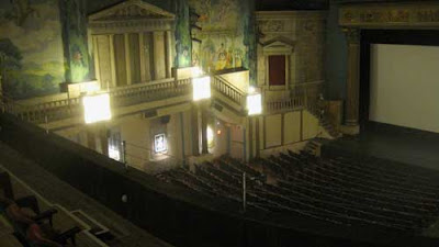 Large theater with painted murals on the far wall and a replica of a Greek temple with columns