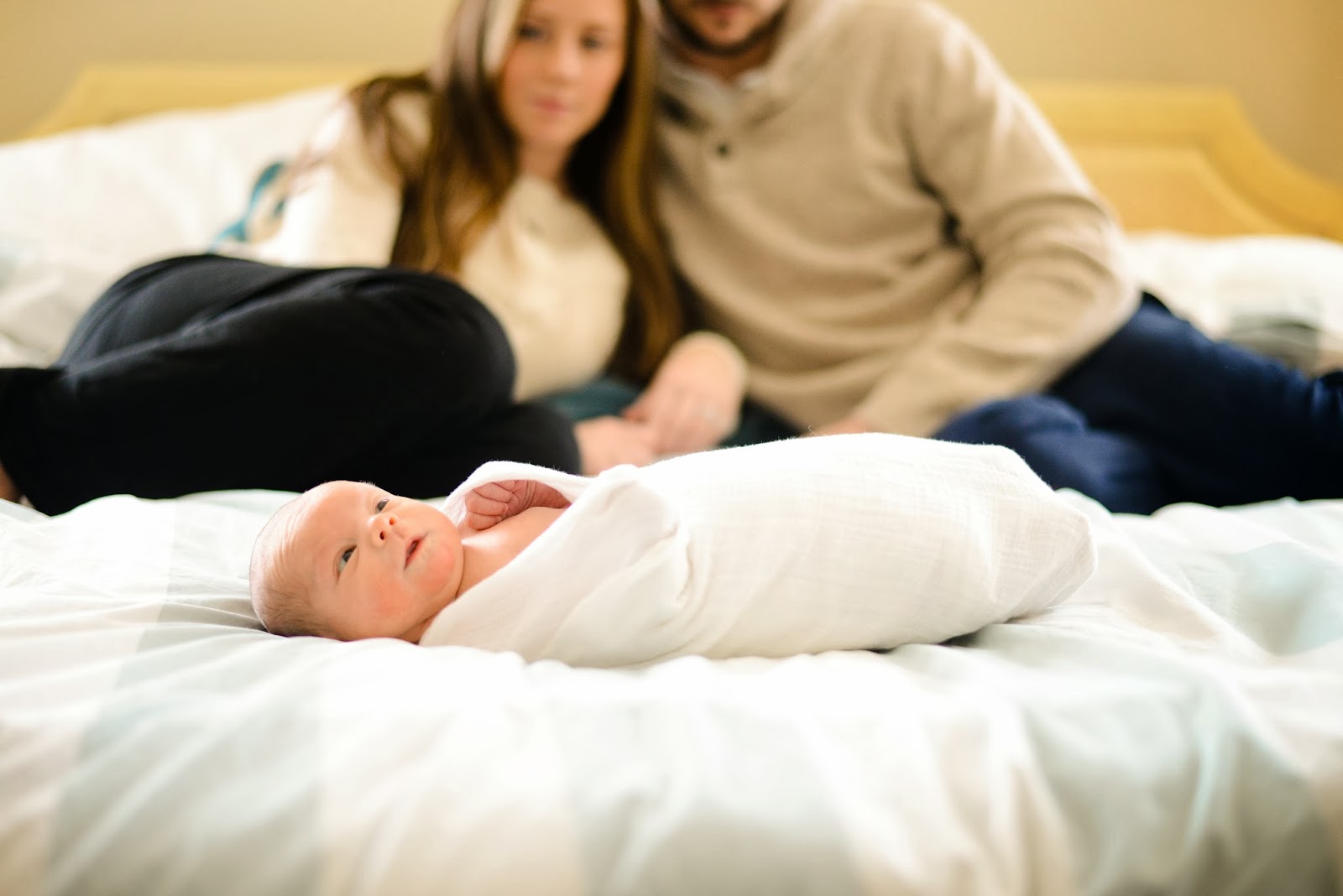 newborn swaddled on bed with Mom and Dad blurred behind