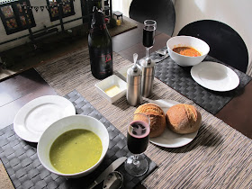 Two bowls od soup (both different), two rolls, and two glasses of sparking shiraz on a dining table.
