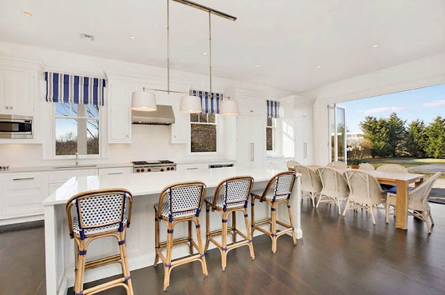 Kitchen with wood floor, cafe chairs, white counters and counter tops and pendant lights with a large door opening up to the backyard