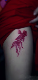 a red gold fish tattoo on the thigh