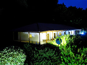 Miniature model of a lit-up building surrounded by bushes, at night.
