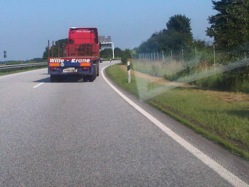 LKW mit schief hängendem Anhänger LKW mit schief hängendem Anhänger, Autobahn, grüne Büsche, blauer Himmel, roter LKW