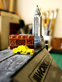 Tiny models of the Chrysler Building, the New York Stock Exchange and a New York yellow cab on top of a table vice.