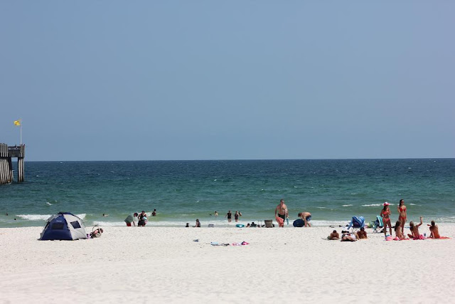 Ankle to shin high waves on Pensacola Beach at Pensacola Beach Gulf Pier with clear blue skies and tourists in the water