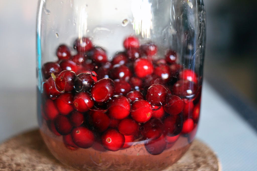 Two cups of fresh cranberries inside a mason jar containing simple syrup.