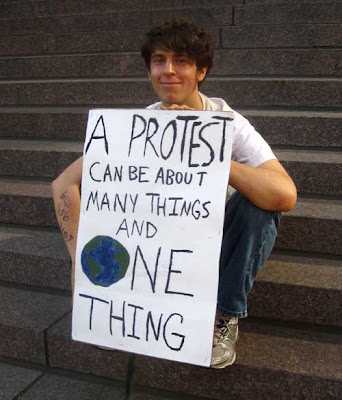 Young man with sign reading A protest can be about many things and ONE THING (with the O in One the planet earth)