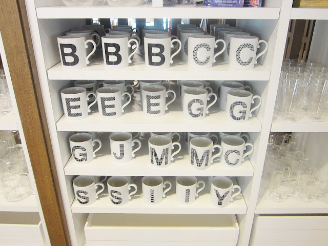 Four shelves holding white alphabet mugs