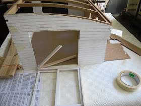 Half-built dolls' house shed with weatherboard cladding attached and a sliding door in pieces in the door frame.