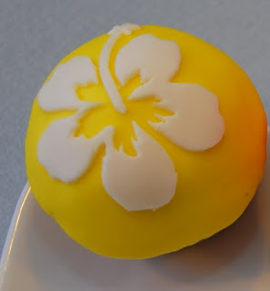yellow fondant cupcake with white hibiscus fondant cutout transferred onto it