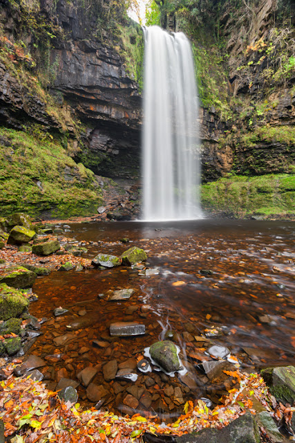 Autumn leaves line the bank at Henrhyd Falls in Wales by Martyn Ferry Photography