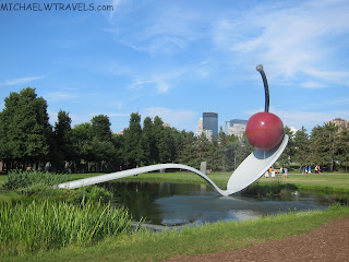 a spoon and cherry sculpture in a park with Minneapolis Sculpture Garden in the background