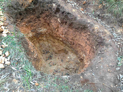 A hole in the ground about 1 metre in diameter and just over one and a half metres deep.