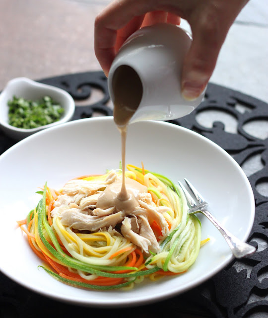 Pouring peanut sauce on bed of vegetable noodles.