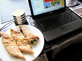 Laptop computer with, on the left, a plate of turkish pide and a mug and, on the right, a biscuit tin and a copy of the magazine The tiny Times.