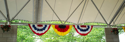 Three flags, two American and one German, hanging between two hanging red begonias.