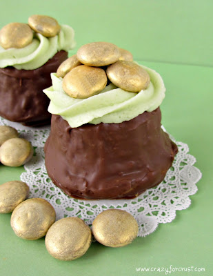 two cupcakes dipped in chocolate with green frosting and gold colored candy to look like pot o gold cupcakes