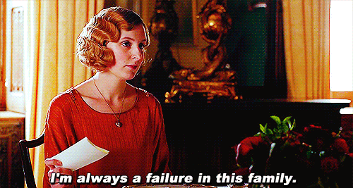 No gif: Lady Edith de Downton Abbey, com um vestido vermelho e uma carta na mão, se levanta da mesa de café, falando "I'm always a failure in this family" em tom sarcástico.
