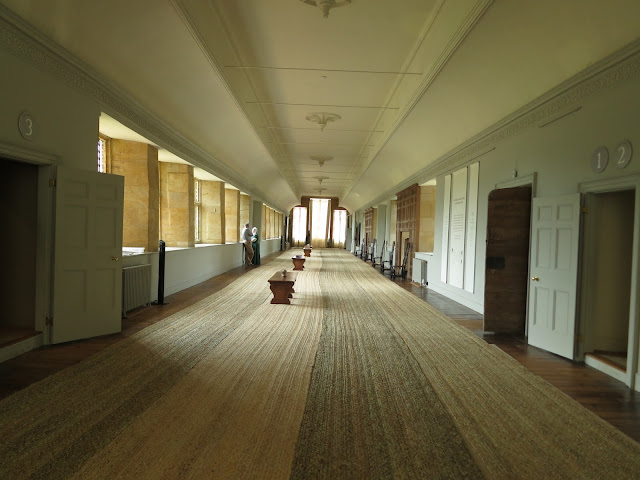 Man talks to woman in historical dress standing by window in long gallery