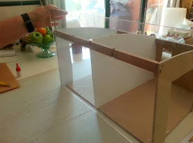 A piece of perspex held up in front of a dry-fitted dolls' house kit.