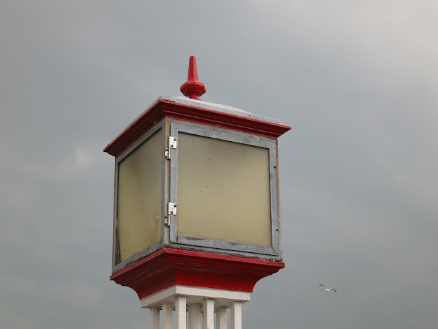Large light that looks like lantern against grey sky with flying gull.