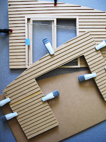 Walls of a dolls' house kit, with weatherboarding clamped to them and a plain wall underneath them.