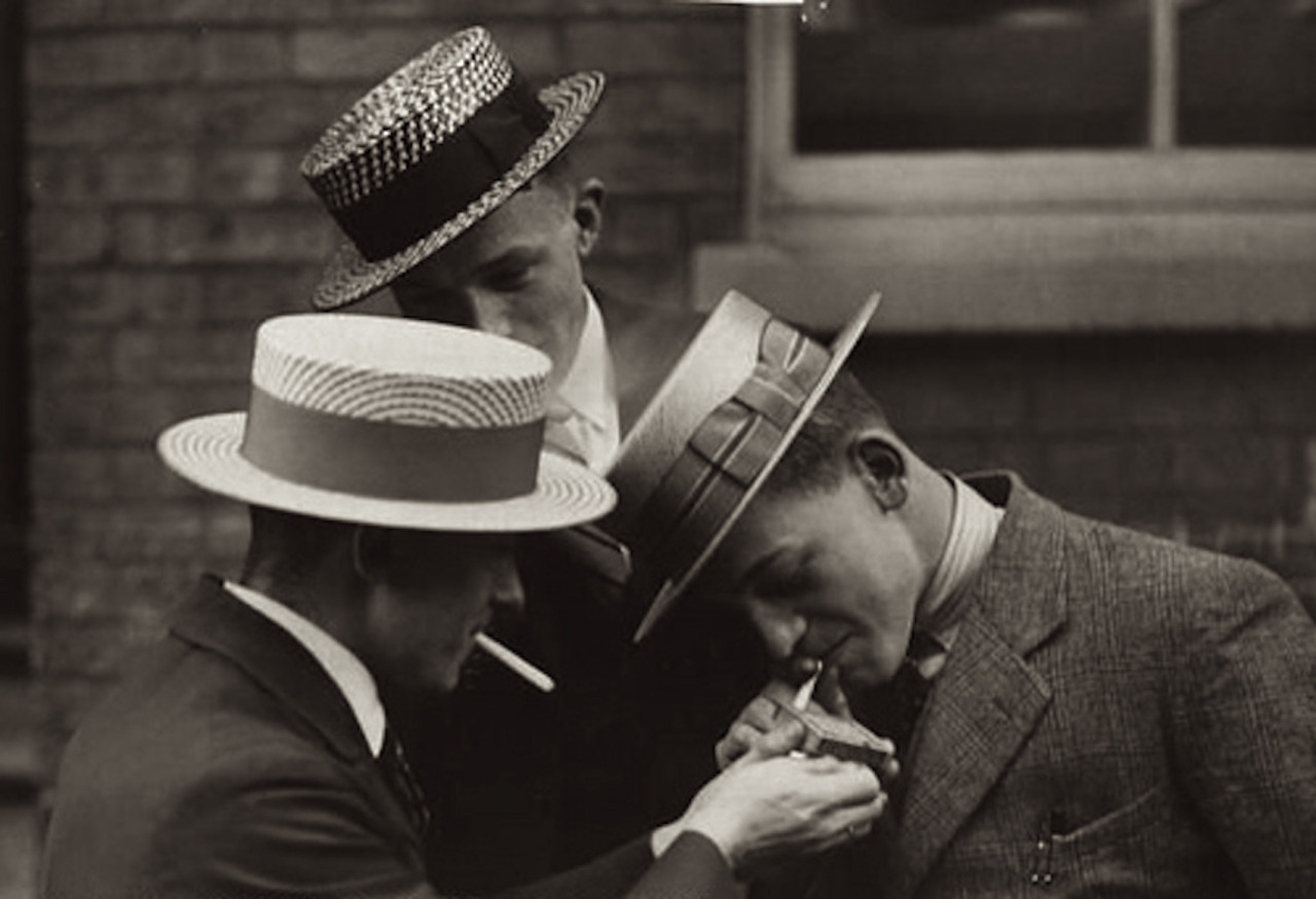 Three youths lighting a cigarette and wearing coloured straw hats known
