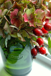 The rich colours of faded hydrangea heads combine well with rosehips.  The up cycled beer bottle vase makes a perfect container!  (from Tuckshopflowers.com)