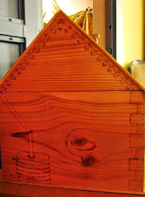 Side of a wooden dolls house, showing pokerwork water barrel and pipe, quoins and iron lace.