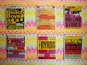 Selection of bright 1960s band posters arranged on a bright, zig zag-patterned wall.