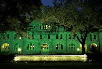 A green lit prestigious stone building at night with an illuminated sign in the front reading Tulane University.
