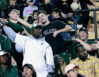 numerous male fans wave while wearing Tulane University gear in the stands of an event.