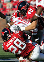 Football players with red mustangs on their blue helmets tackle an opposing player in a game.