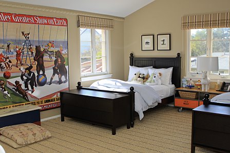Kids bedroom with dark wood beds with trunks at the foot, a large circus poster and striped roman shades