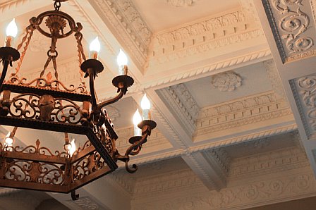 Original ornate coffered ceiling and a large Spanish iron chandelier in a living room after remodeling