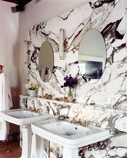 Bathroom with veiny marble for the wall of the sink, pedestal sinks and round mirrors