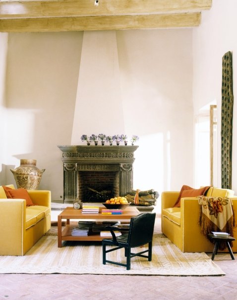 Living room with large dueling yellow upholstered sofas, a wood coffee table, visible natural wood beams and a carved fireplace 