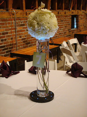 Centerpieces composed of football mum pomanders placed atop tall cylinder 