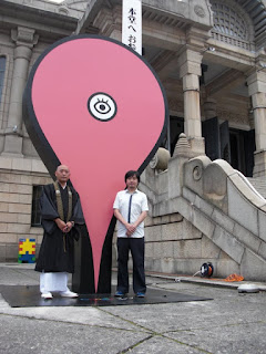築地本願寺に設置されたGoogle マップピンの前で写真を撮る坊さんを示す画像。
