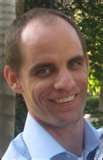 Photo from opentext.com This is a picture of Michael Wesch in a blue shirt and he seems to be standing with his back against the edge of a building with many trees in the background.